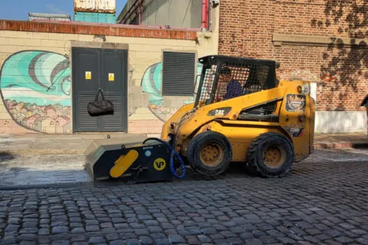 Barredora industrial en minicargadora barriendo calle